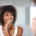A young woman with curly brown hair brushing her teeth in the mirror