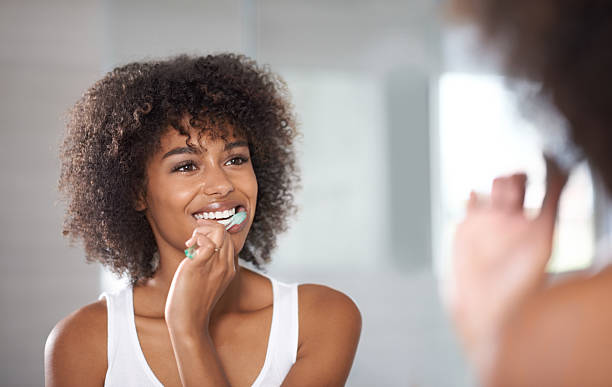 A young woman with curly brown hair brushing her teeth in the mirror