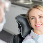A young blonde woman speaking with her dentist in the dental chair
