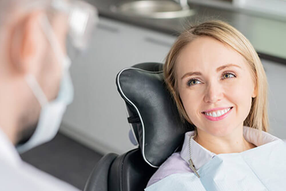 A young blonde woman speaking with her dentist in the dental chair