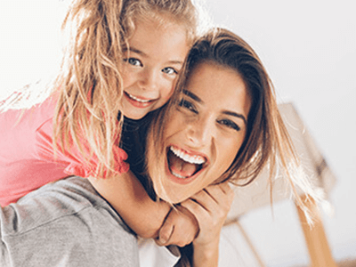 Mom with young daughter on her back smiling for the camera