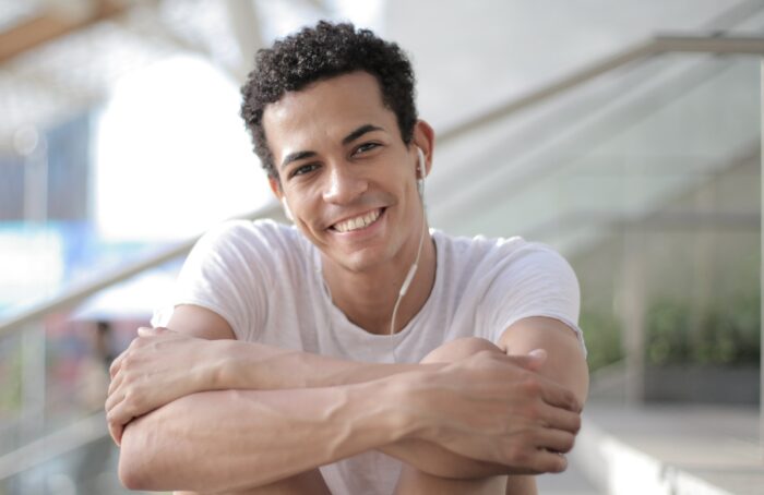 A young man with dark hair smiling at the camera with headphones in