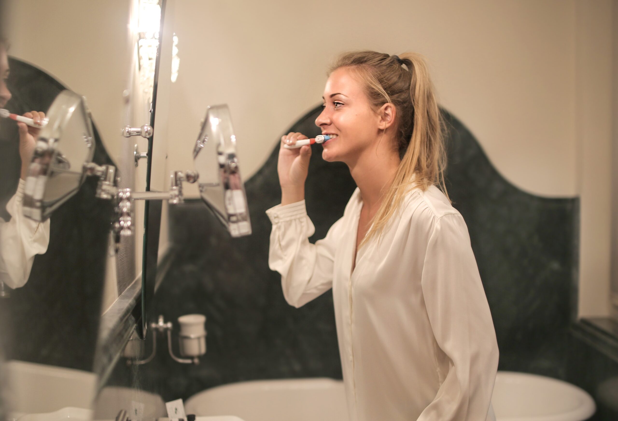 A blonde woman standing in front of the bathroom mirror brushing her teeth