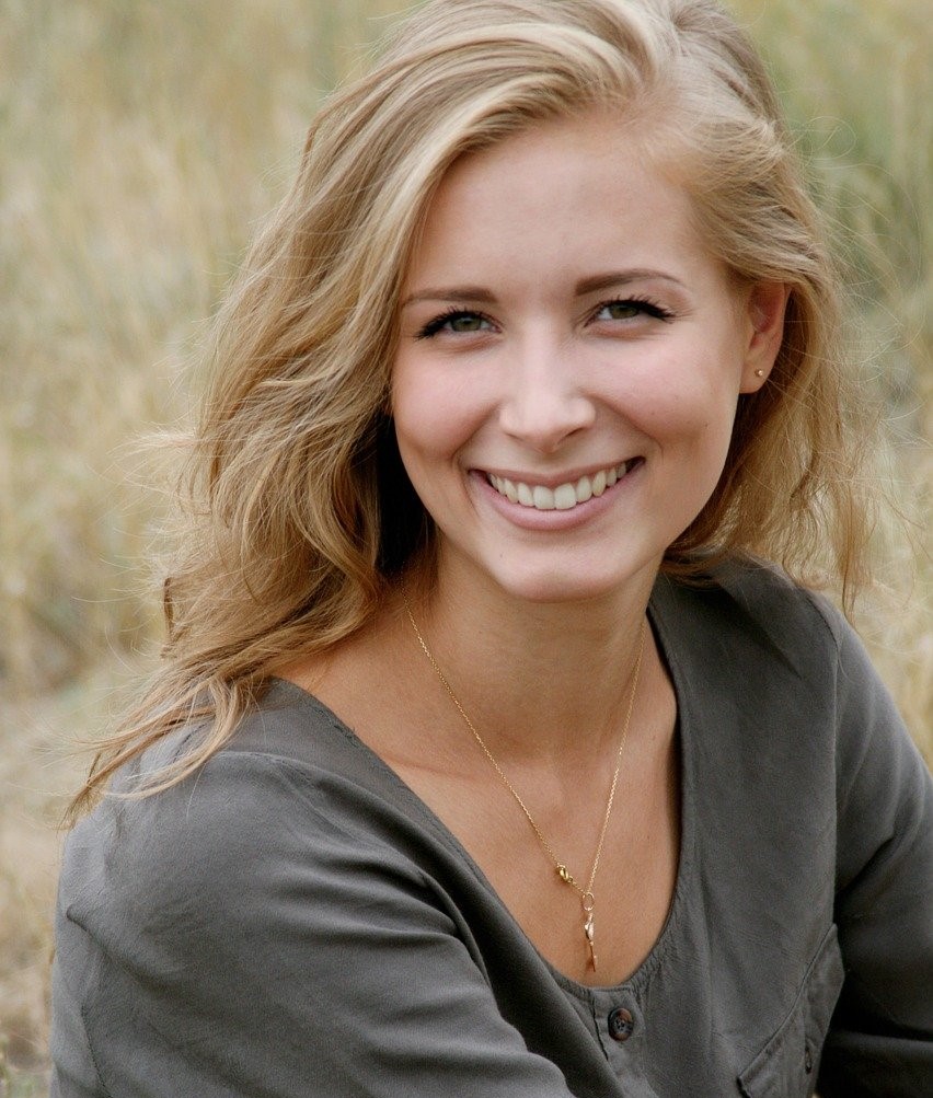 Woman with blonde hair sitting in the grass and smiling