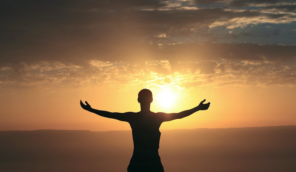 A woman staring into the sun with arms open