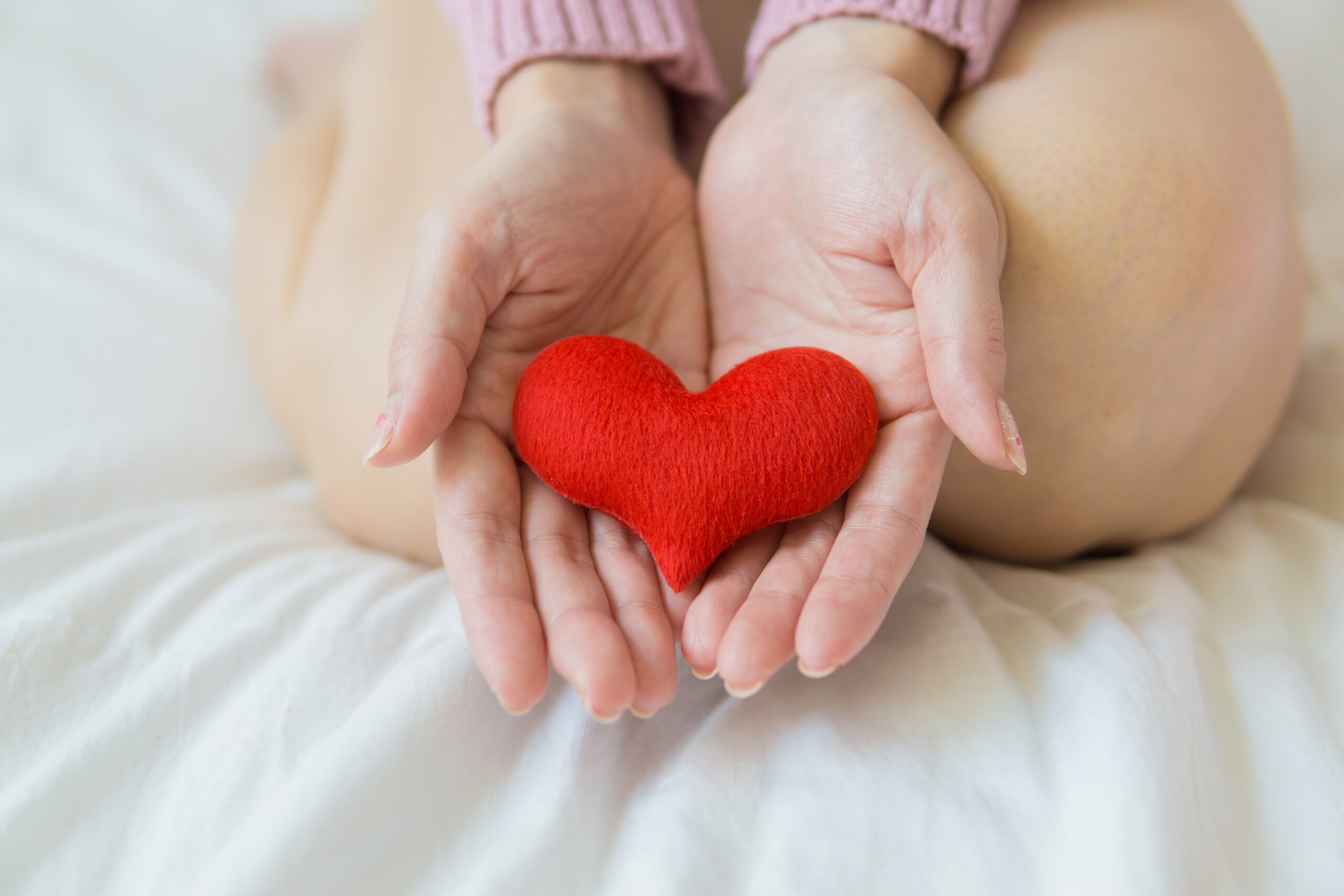 A woman kneeling on the bed with a sewn, red heart in her hand