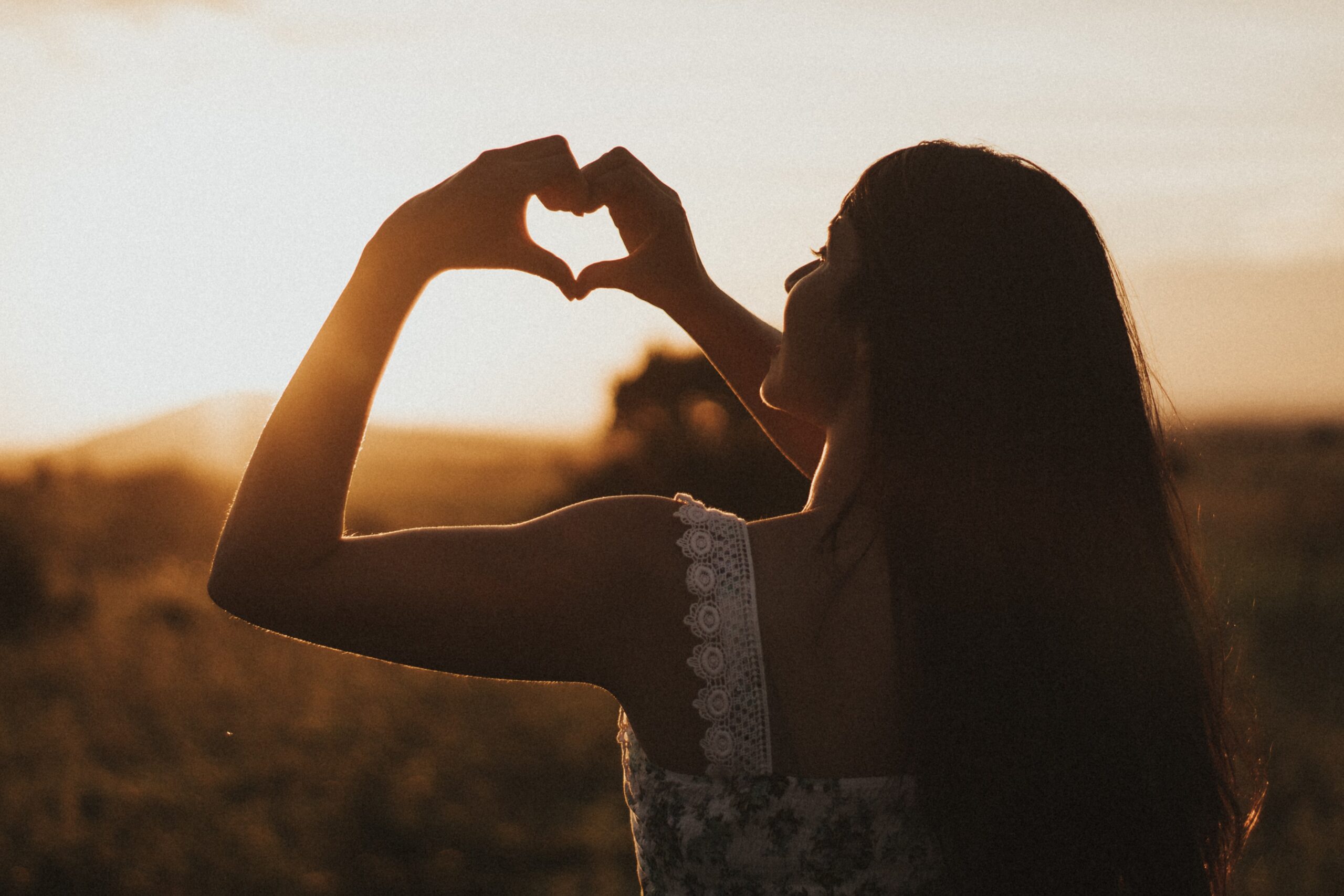 Woman standing in the setting sun forming a heart with her hands