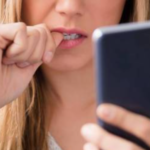A blonde woman staring at her phone and biting her fingernails