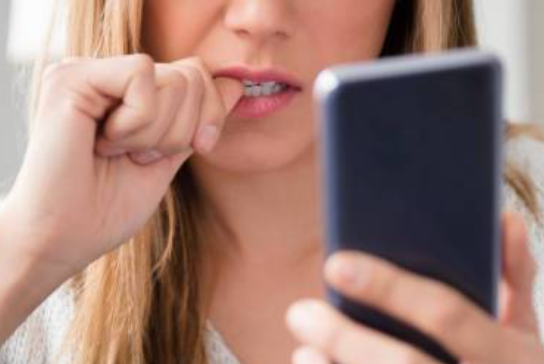 A blonde woman staring at her phone and biting her fingernails