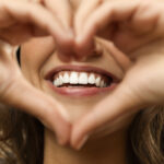 Closeup of a woman holding her hands in a heart-shape in front of her beautiful smile