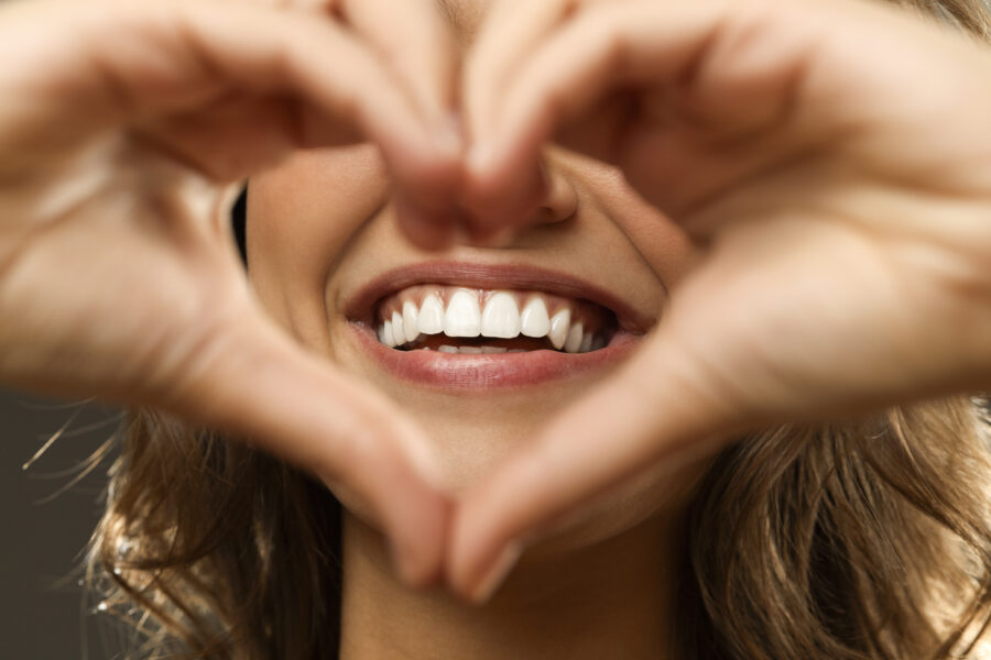 Closeup of a woman holding her hands in a heart-shape in front of her beautiful smile