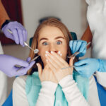 photograph of woman in dental chair blocking her mouth, delay dental treatment, consequences