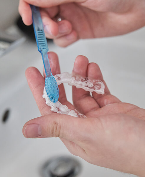 person brushing a clear aligner with a toothbrush